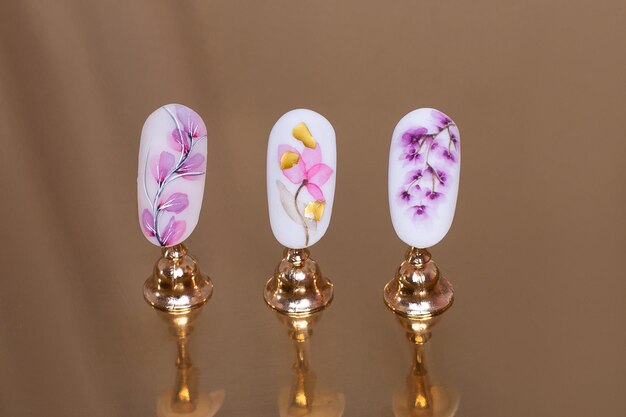 Hermosas muestras de uñas con diseño floral sobre fondo dorado. Enfoque suave.