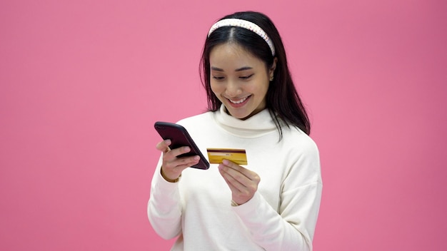Hermosas mujeres de Asia sonríen, usan teléfonos inteligentes y compras con tarjeta de crédito, compran en línea y se emocionan con el pago exitoso en un fondo rosa aislado
