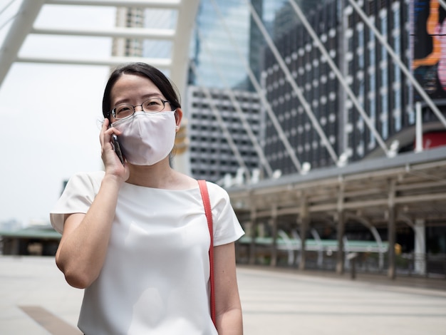 Hermosas mujeres asiáticas con mascarilla médica desechable, usando un teléfono inteligente en un área pública, en la carretera o en el centro de la ciudad, como una nueva tendencia normal