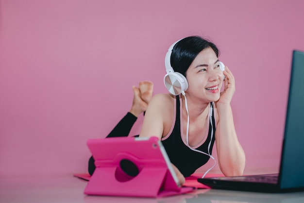 Hermosas mujeres asiáticas usan auriculares, hacen ejercicio en ropa deportiva negra, se acuestan, ven videos de ejercicios en el hogar y computadoras portátiles.