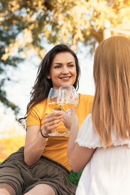 Hermosas mujeres bebiendo vino en el parque. Amigos y concepto de verano.