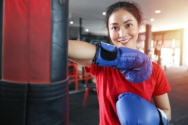 Hermosas mujeres boxeadoras asiáticas felices y divertidas fitness boxeando y golpeando una bolsa con guantes de boxeo