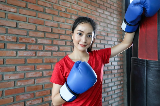 Hermosas mujeres boxeadoras asiáticas felices y divertidas fitness boxeando y golpeando una bolsa con guantes de boxeo