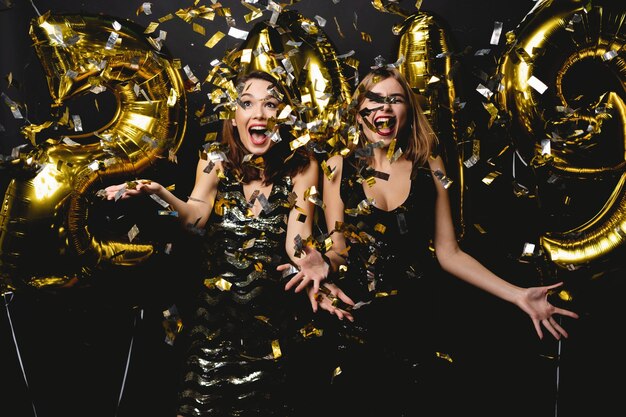 Hermosas mujeres celebrando el año nuevo. Chicas hermosas felices en elegantes vestidos de fiesta sexy con globos de oro 2019, divirtiéndose en la fiesta de fin de año. Celebración navideña. Imagen de alta calidad