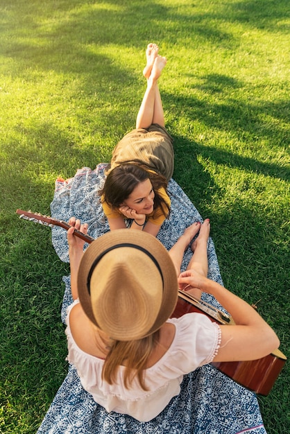 Hermosas mujeres divirtiéndose tocando la guitarra en el parque. Amigos y concepto de verano.