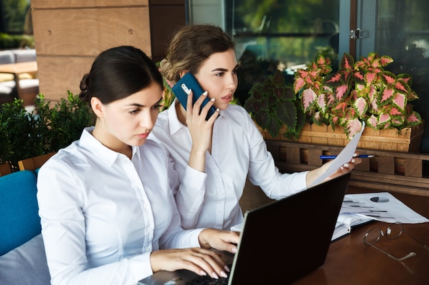 Hermosas mujeres empresarias jóvenes trabajando en equipo portátil en el café de la calle al aire libre