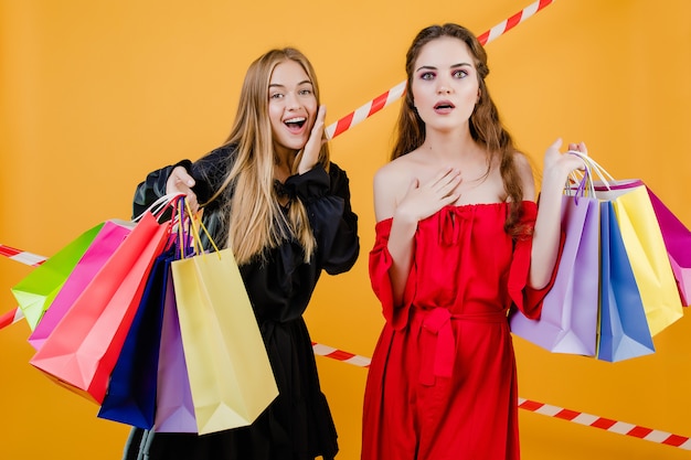 Hermosas mujeres jóvenes con coloridos bolsos de compras y cinta de señal aislada sobre amarillo