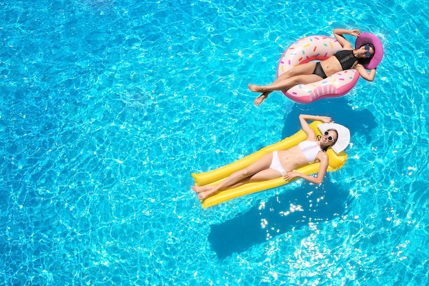 Hermosas mujeres jóvenes con donut inflable y colchón en piscina azul