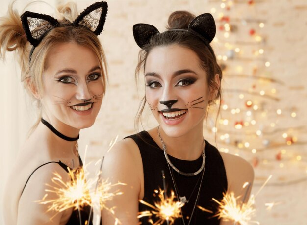 Hermosas mujeres jóvenes con maquillaje de gato y luces de bengala en la fiesta
