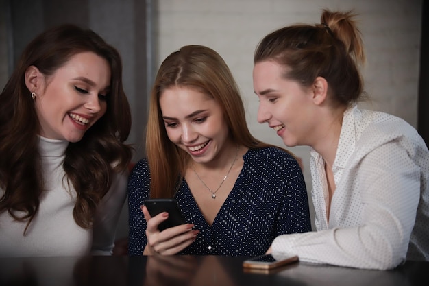 Hermosas mujeres jóvenes sentadas en un bar mirando el teléfono sonriendo