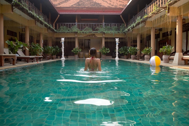 Hermosas mujeres relajándose en la piscina de lujo Chica en la piscina del resort de spa de viaje Vacaciones de lujo de verano Hotel en estilo tailandés tradicional descansando en una vista exótica desde la parte posterior