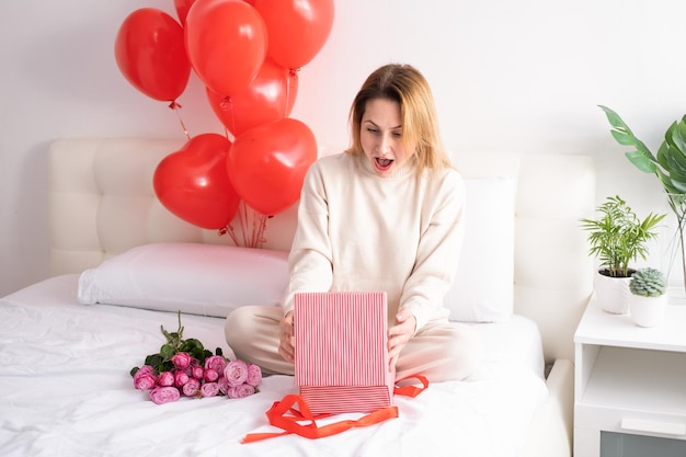 Hermosas mujeres en ropa informal acogedora con caja de regalo y globos en la cama celebrando el día de san valentín