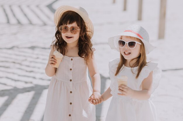 Hermosas niñas con vestido blanco y sombrero comiendo helado en la playa en verano