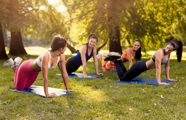 Hermosas novias haciendo ejercicio de flexiones en el parque con entrenadora de fitness femenina. Enfoque selectivo.