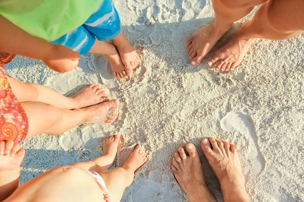 Hermosas piernas familiares en la arena junto al mar