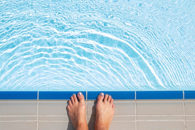 Hermosas piernas femeninas al borde de la piscina azul