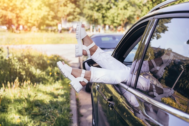 Hermosas piernas femeninas con botas blancas y jeans colgando de la ventana del coche