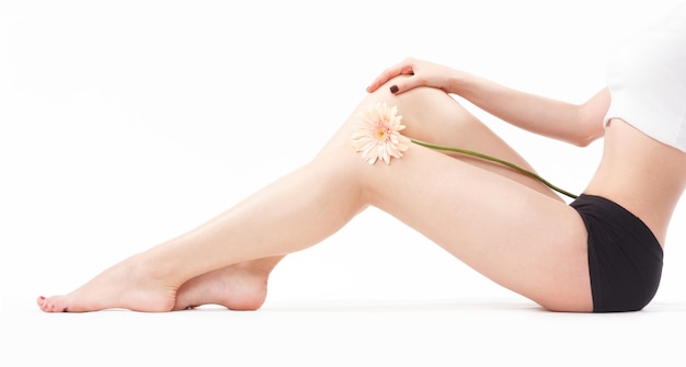 Hermosas piernas femeninas con flor de gerbera rosa aislada sobre fondo blanco