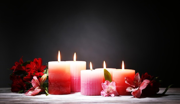 Hermosas velas con flores en la mesa de madera, sobre fondo oscuro