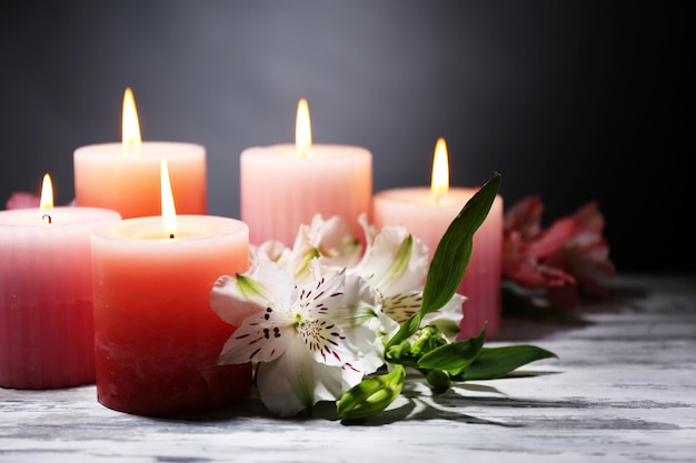 Hermosas velas con flores en la mesa de madera, sobre fondo oscuro
