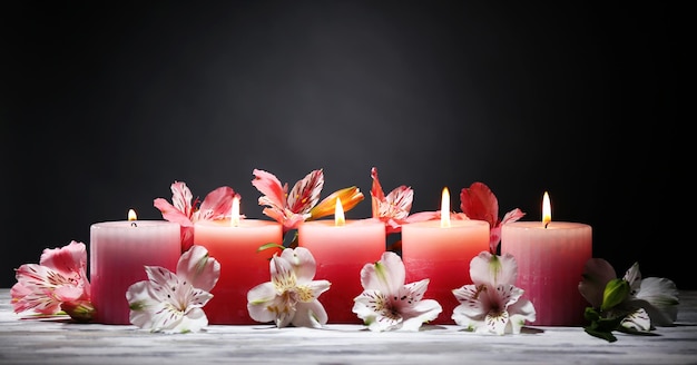 Hermosas velas con flores en la mesa de madera, sobre fondo oscuro