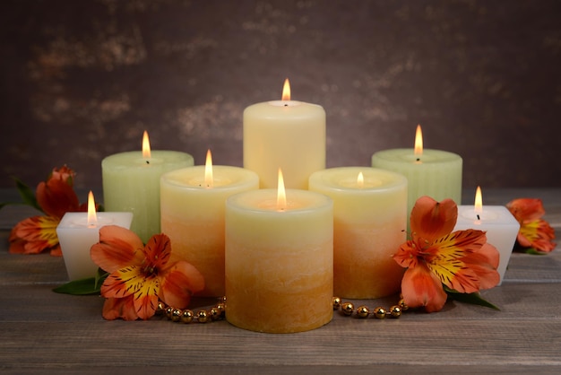 Hermosas velas con flores en la mesa sobre fondo marrón