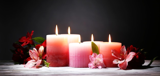 Hermosas velas con flores sobre mesa de madera, sobre fondo oscuro