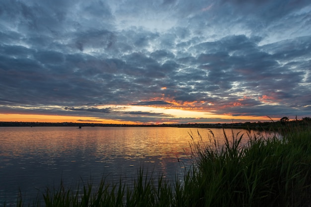 Hermoso amanecer en el río, antes del amanecer, con parte de la orilla y cañas