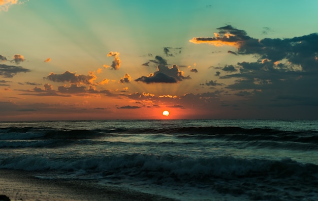 Hermoso amanecer sobre el mar azul. rayos brillantes del sol. olas en la playa.