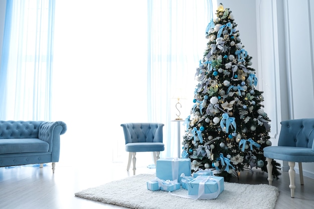 Hermoso árbol de Navidad con decoración azul en una habitación blanca.