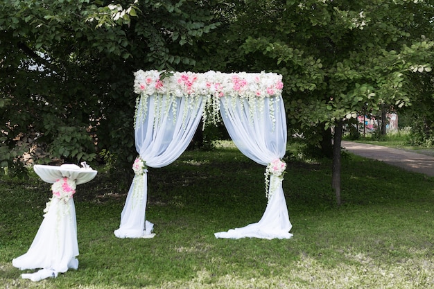 Hermoso arco blanco con adornos florales para la ceremonia de la boda con sillas para invitados en el fondo verde con árboles