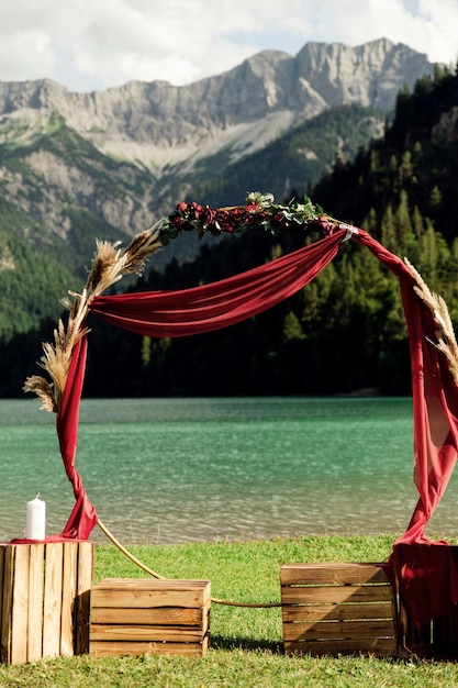 Foto un hermoso arco de bodas con dos sillas para la novia y el novio contra el telón de fondo de las montañas alpinas y la ceremonia de bodas del lago en un prado en los alpes