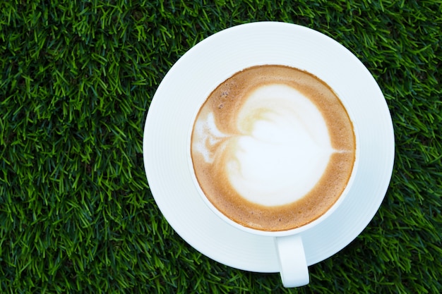 Hermoso arte de café con leche caliente en taza blanca sobre fondo verde hierba