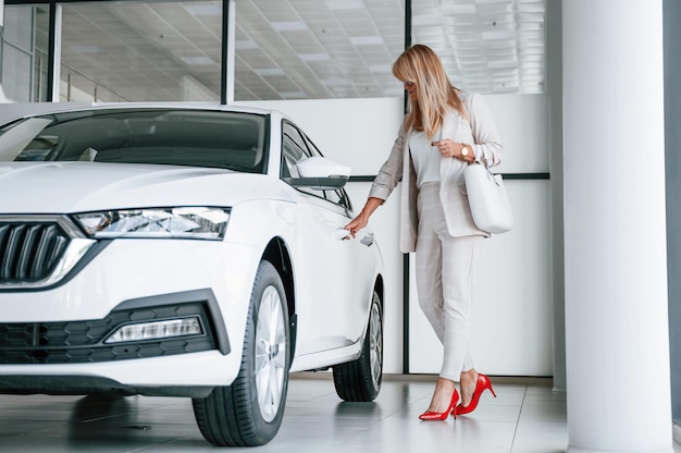 Con un hermoso automóvil nuevo La mujer con ropa formal blanca está en el concesionario de automóviles