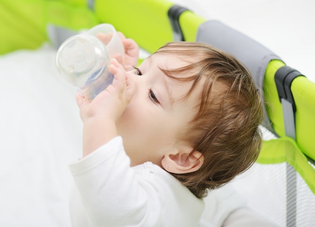 Hermoso bebé con una botella de leche en la cama