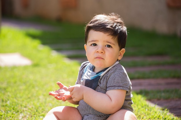 Hermoso bebé brasileño en la hierba mirando a cámara. Bebé serio.