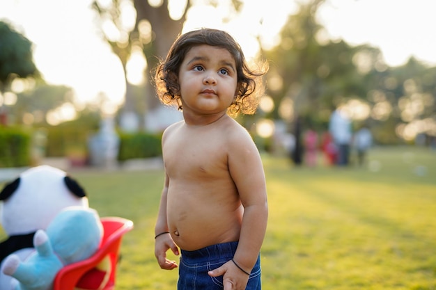 Hermoso bebé con cabello rizado en el jardín sin camiseta