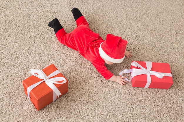 Hermoso bebé celebra la Navidad. Vacaciones de año nuevo. Bebé en traje de Navidad y gorro de Papá Noel y caja de regalo, vista superior.
