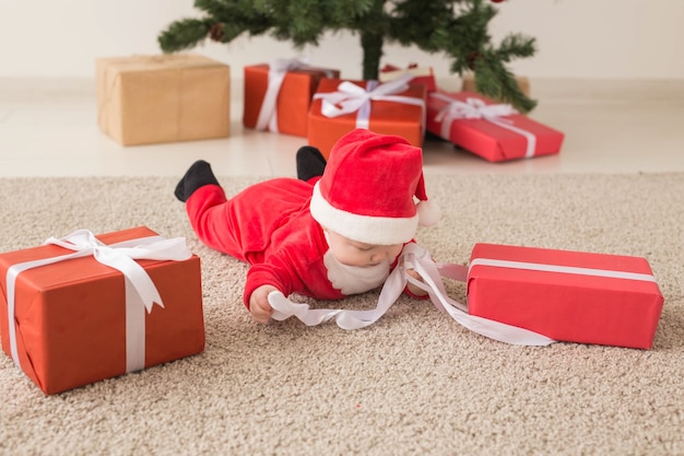 Hermoso bebé celebra la Navidad. Vacaciones de año nuevo. Bebé en traje de Navidad y gorro de Papá Noel y caja de regalo, vista superior.