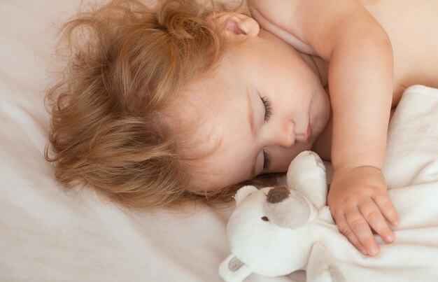 Hermoso bebé durmiendo en la cama en casa con un niño de juguete durmiendo en la cama