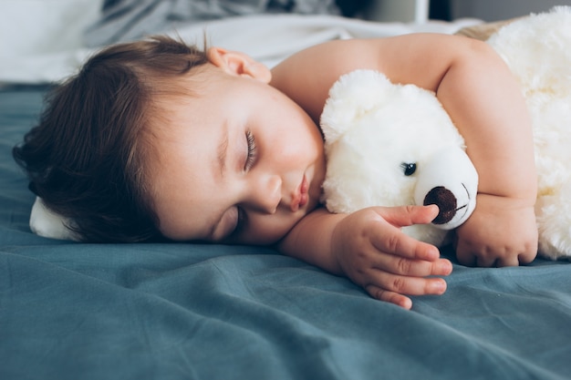 Hermoso bebé durmiendo con su osito de peluche a un lado, concepto de familia