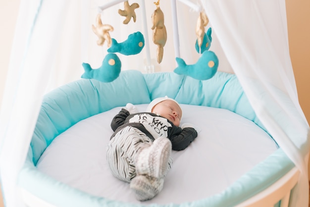 Hermoso bebé recién nacido acostado en una cama ovalada con hermosos parachoques en delicados tonos grises, azules y blancos