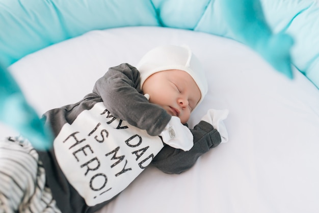 Hermoso bebé recién nacido acostado en una cama ovalada con hermosos parachoques en delicados tonos grises, azules y blancos