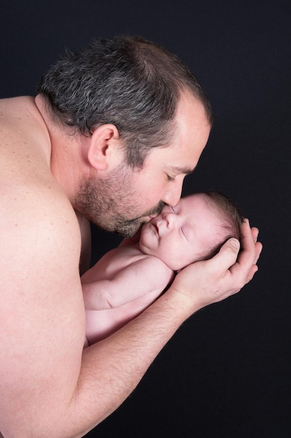 Hermoso bebé recién nacido besando a su padre con un fondo negro