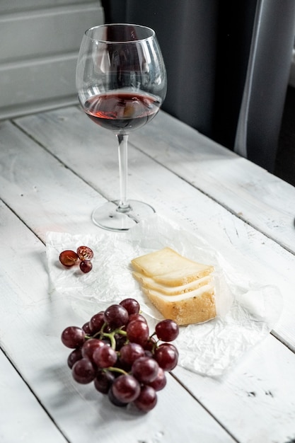 Hermoso bodegón con un duro trozo de queso y vino tinto en un vaso sobre un fondo de madera blanca.