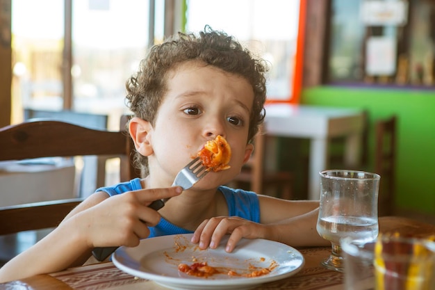 Foto hermoso chico de pelo rizado comiendo tortellini en el restaurante