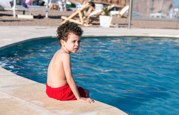 Hermoso chico sentado al borde de la piscina