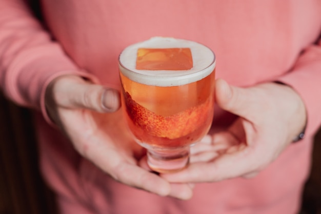 Un hermoso cóctel rosado con un gran cubo de hielo en un vaso bajo, adornado con ralladura de naranja sanguina