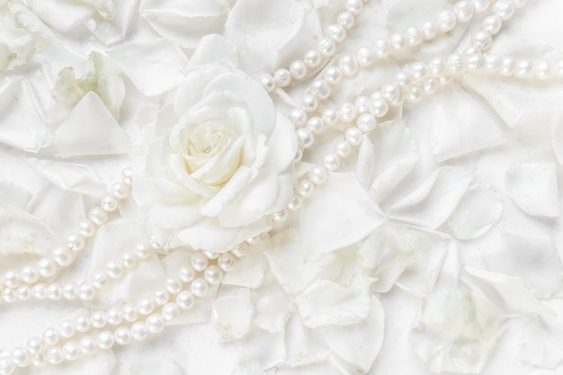 Foto hermoso collar de perlas y rosas blancas sobre un fondo de pétalos ideal para tarjetas de felicitación para