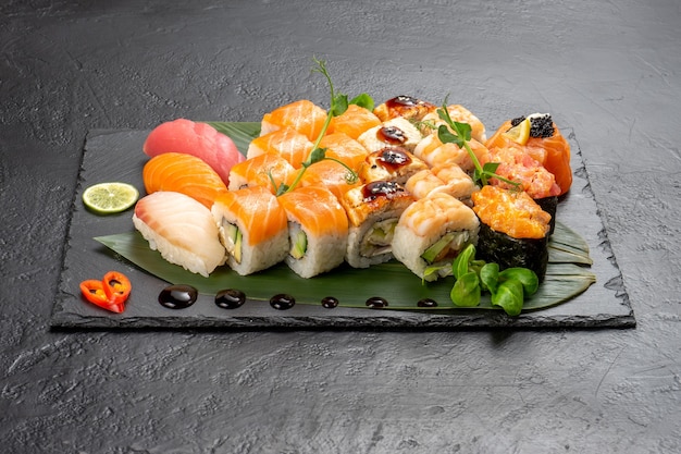 Hermoso conjunto grande de diferentes tipos de sushi maki y nigiri en una placa de pizarra de piedra rectangular negra.